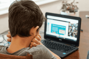 Boy watching online class on Dell laptop, wearing a gray shirt.