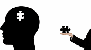 Silhouette head with puzzle piece, hand holding piece, black and white illustration.
