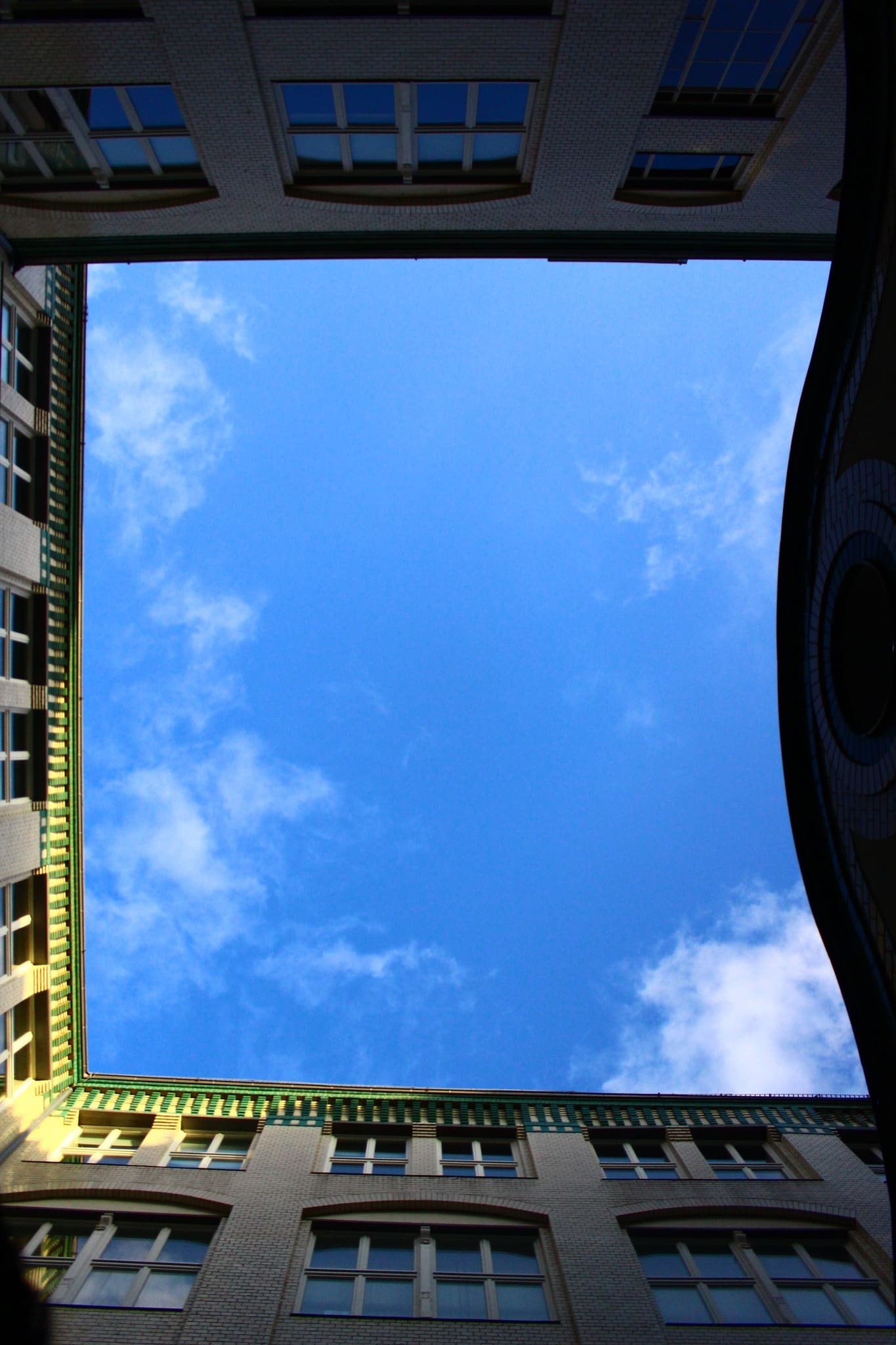 Upward view of building courtyard framing blue sky with scattered clouds.