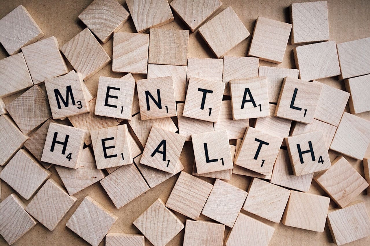 Wooden tiles spelling "MENTAL HEALTH" on scattered blank tiles, photo style.