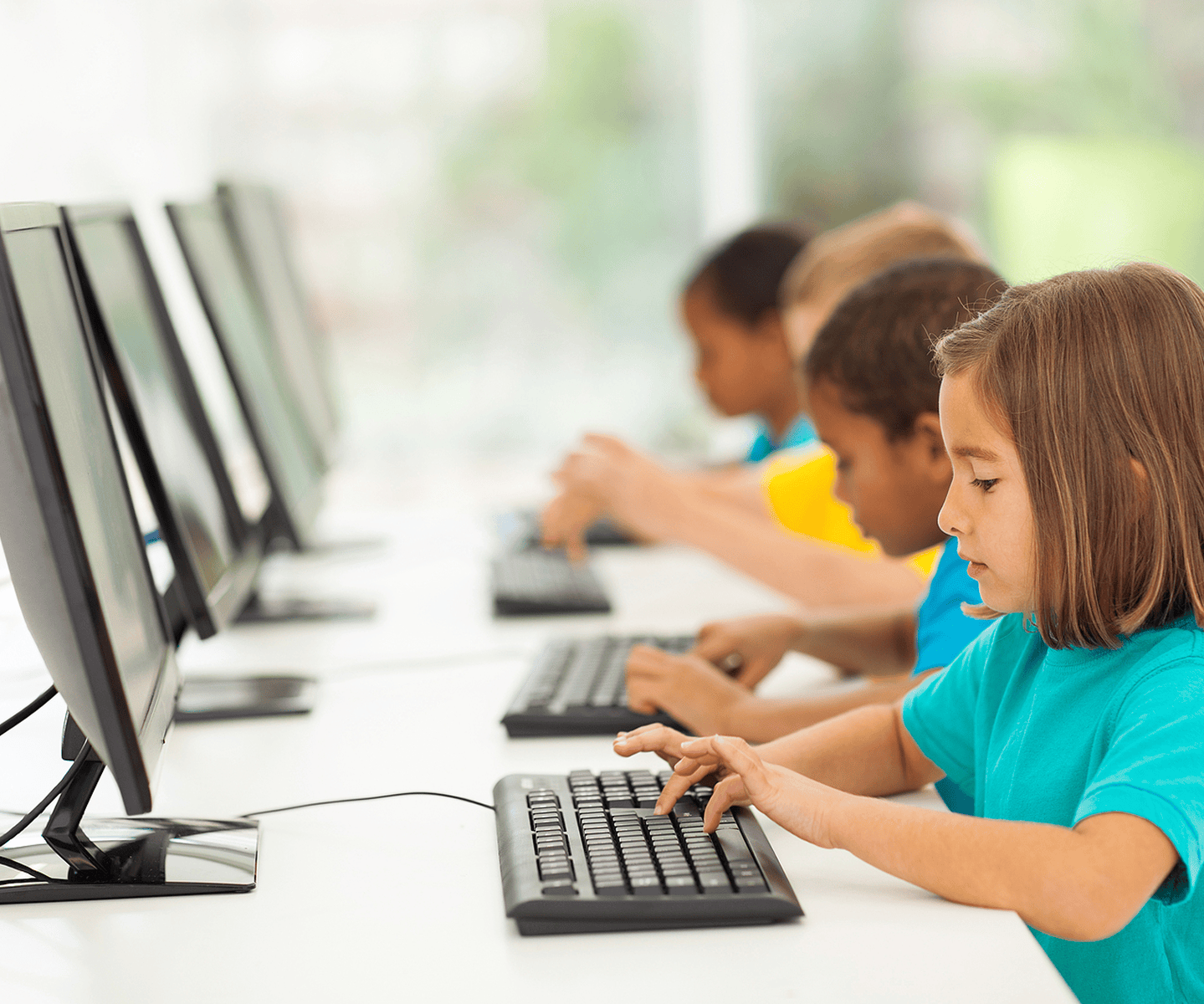 Elementary students typing on keyboards at a row of classroom computers